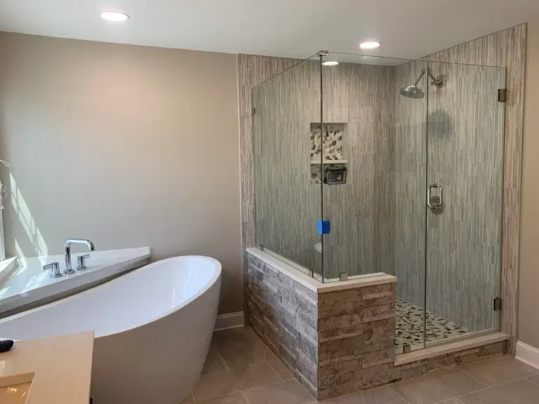 Frameless corner shower enclosure in travertine tile next to a freestanding soaking tub