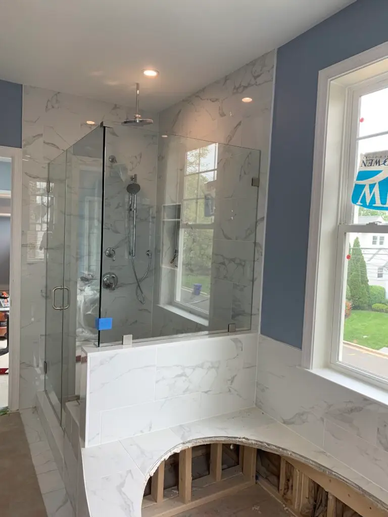 Frameless glass shower enclosure with inline door and fixed panel beside a freestanding tub