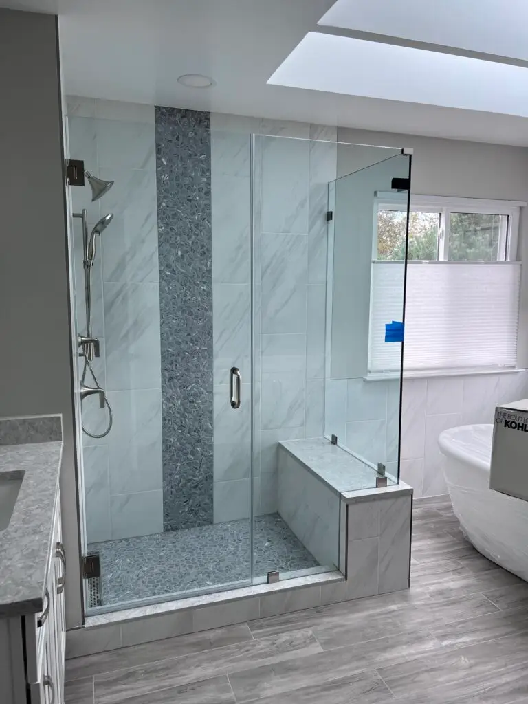 Frameless shower enclosure set on a tiled knee wall with a mosaic accent band