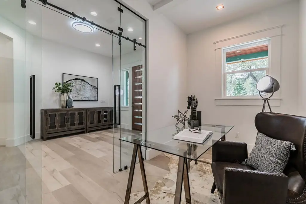 Frameless glass sliding door on a black barn-door track in a home office