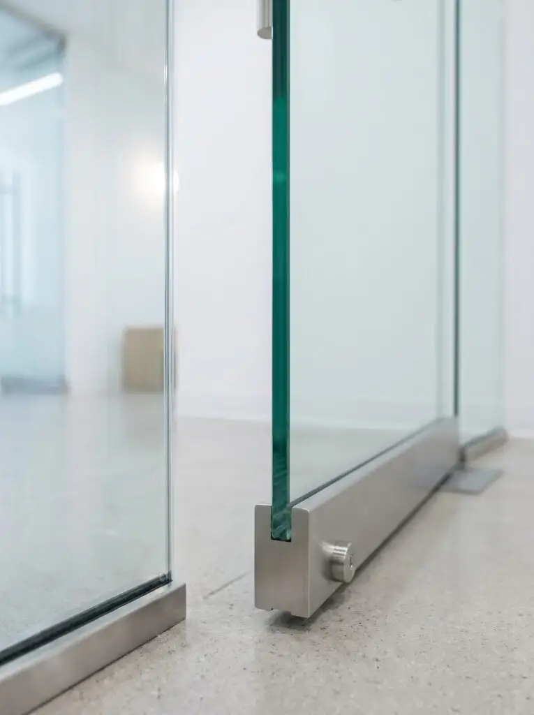 Close-up of a stainless bottom rail, patch fitting and cylinder lock on a frameless all glass door