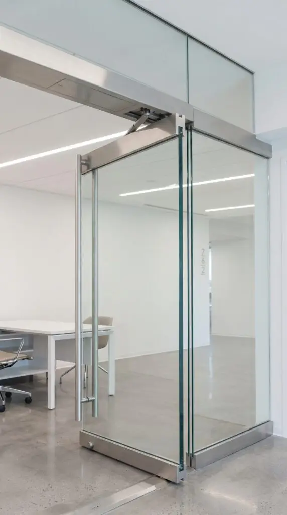 Stainless header with the concealed overhead closer arm, top rail, bottom rail and pivot on a frameless all glass office door