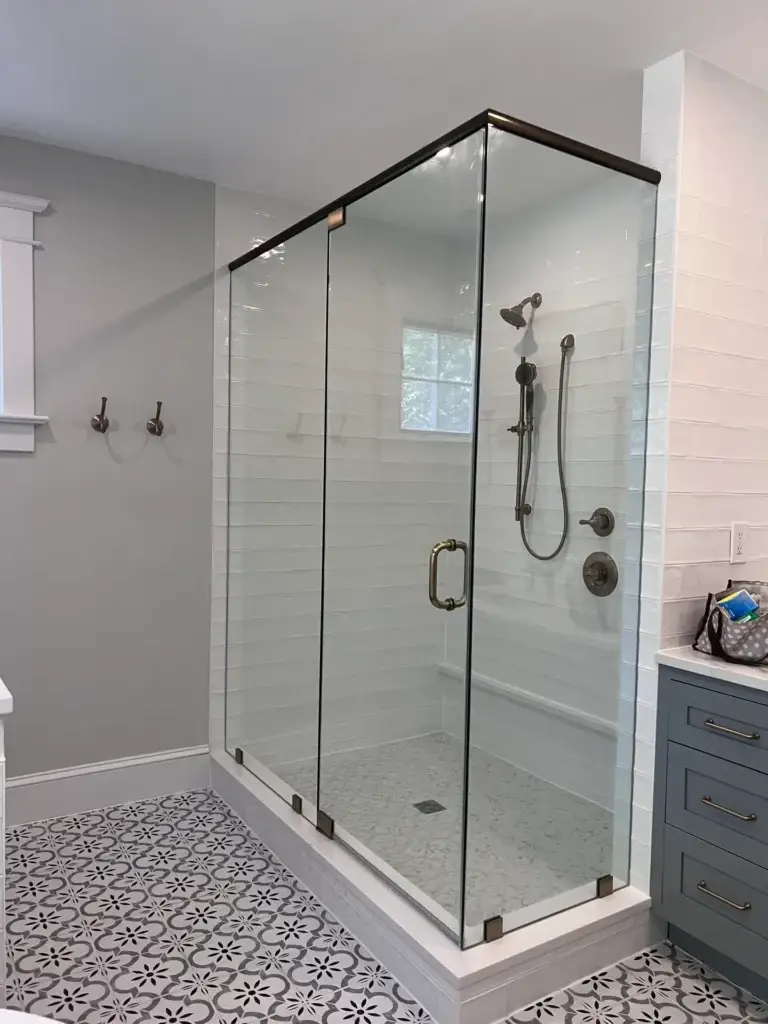 Frameless glass corner shower with a black header above a patterned tile floor