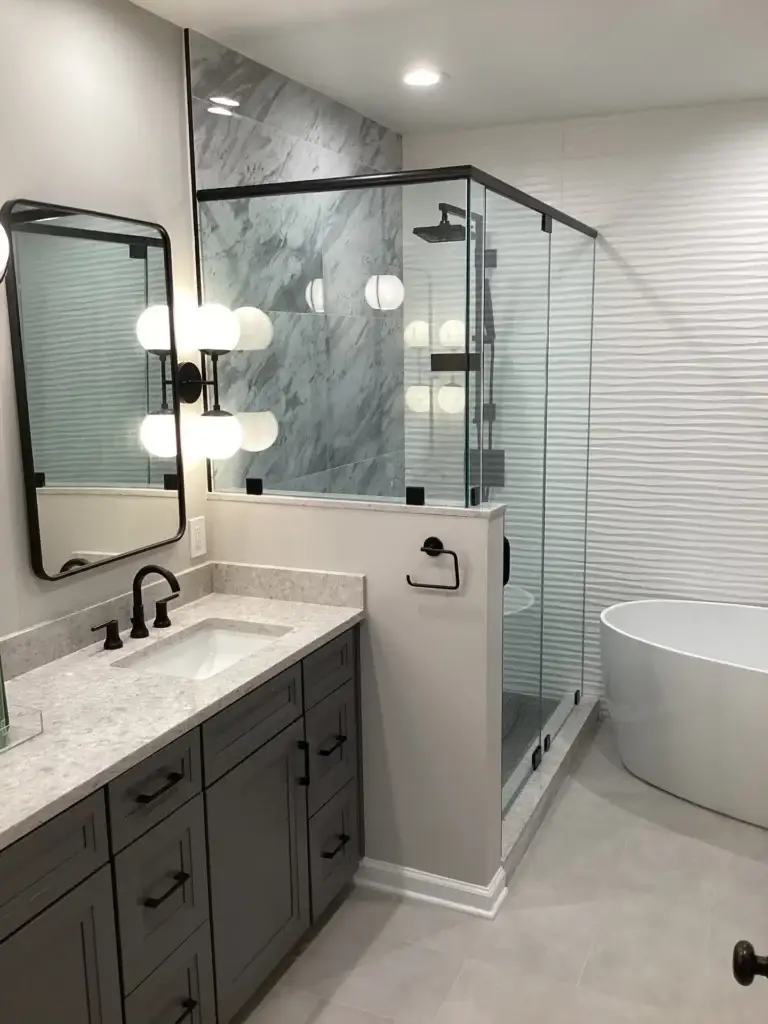 Frameless glass shower on a knee wall with black hardware in a grey marble-look bathroom