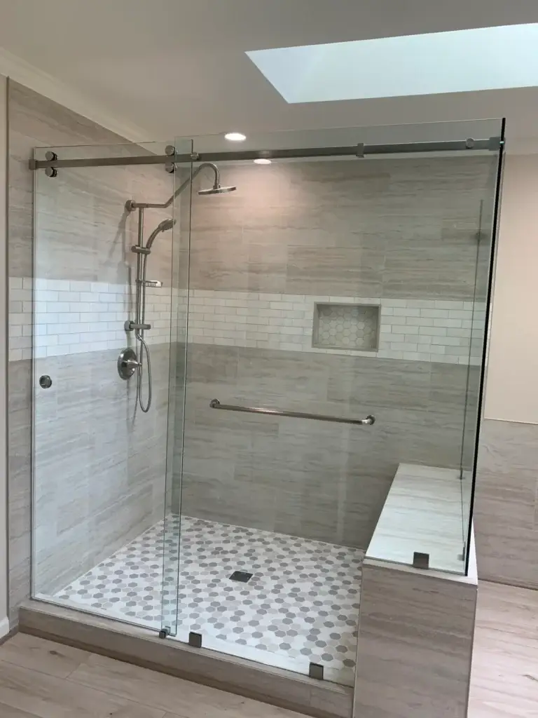 Frameless sliding shower door with a glass panel on a tiled bench, under a skylight