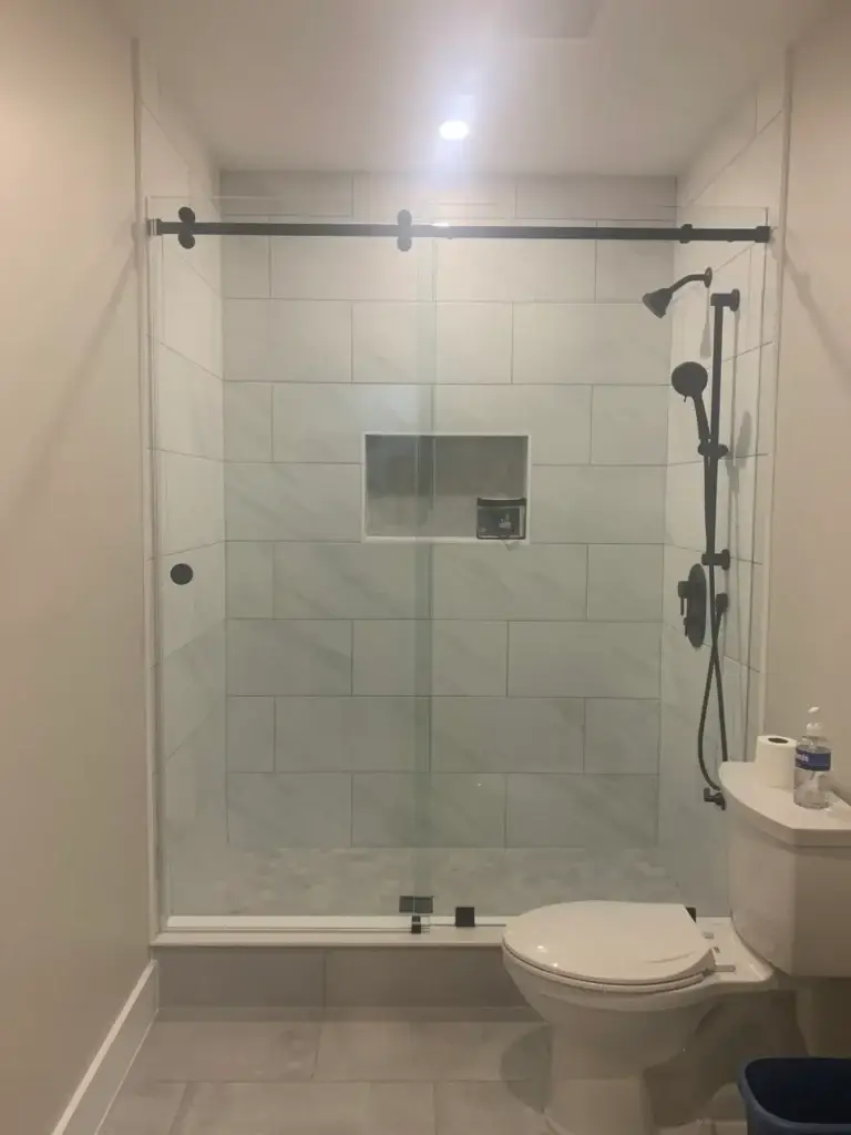 Frameless sliding shower door with a dark-finish rail in a white marble-look tile shower