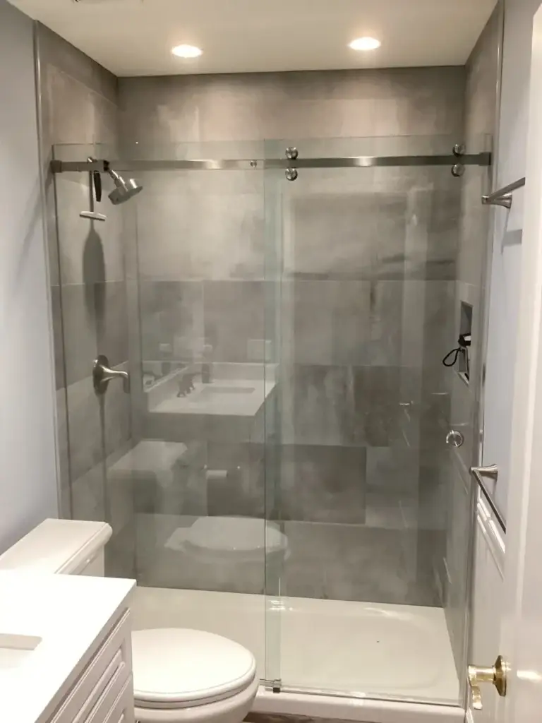 Frameless sliding shower door over a shower base in a grey large-format tile shower