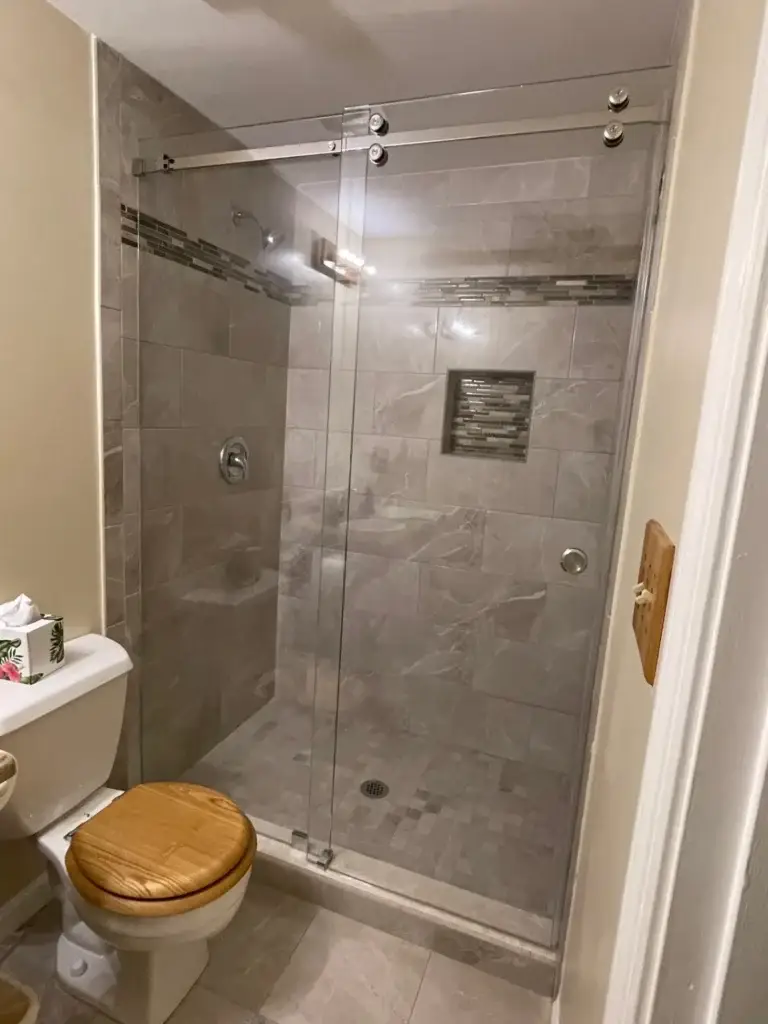Frameless sliding shower door in a grey tile shower with a mosaic accent band