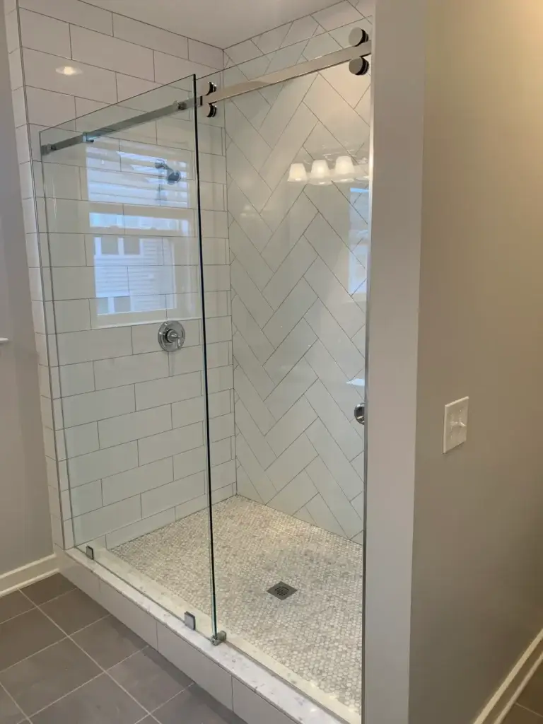 Frameless sliding shower door in a white herringbone subway tile shower with a mosaic floor