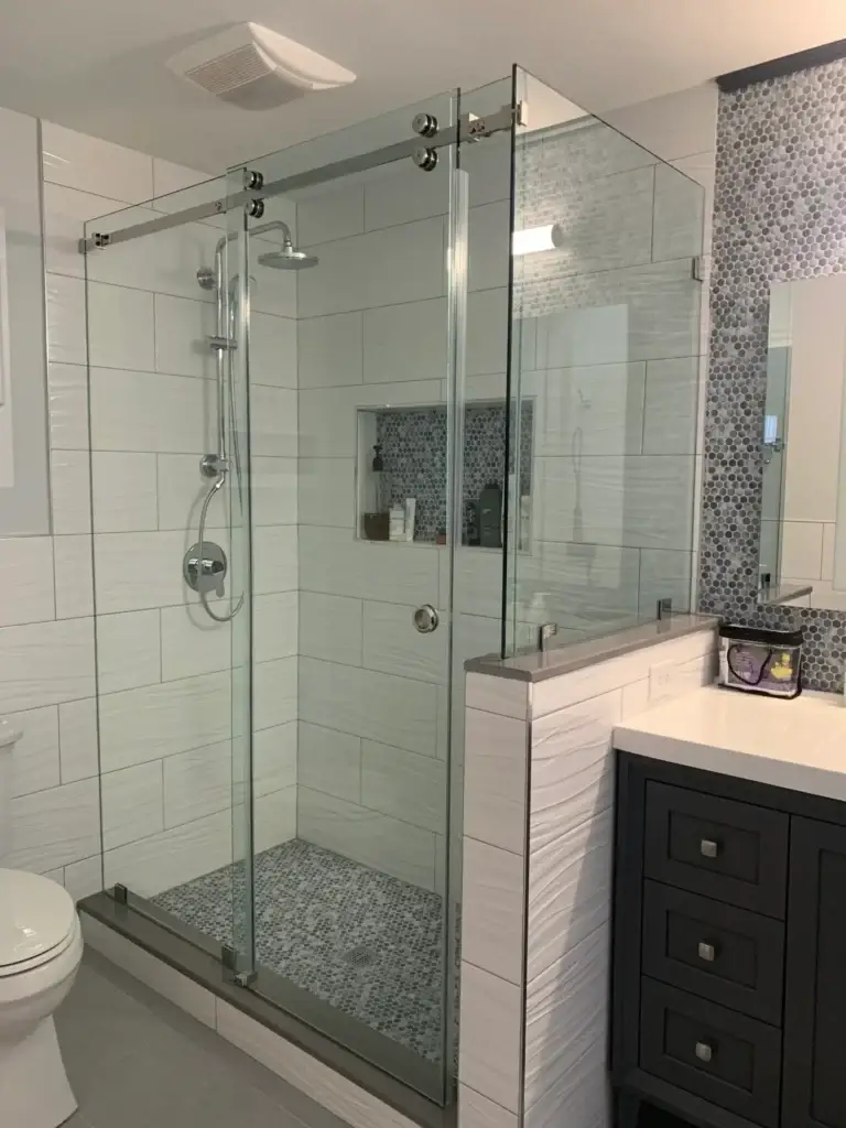 Frameless sliding shower door with a return panel on a tiled knee wall and a pebble floor