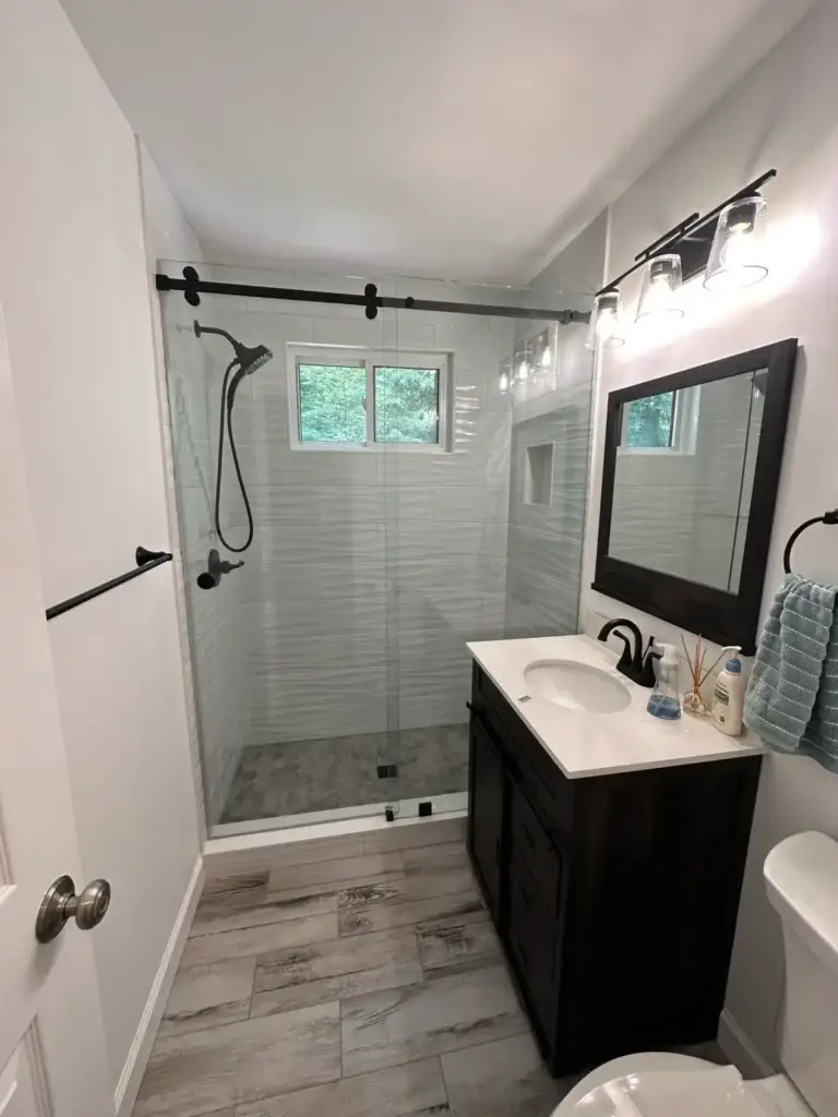 Frameless sliding shower door with a matte black rail across a tiled shower alcove with a window