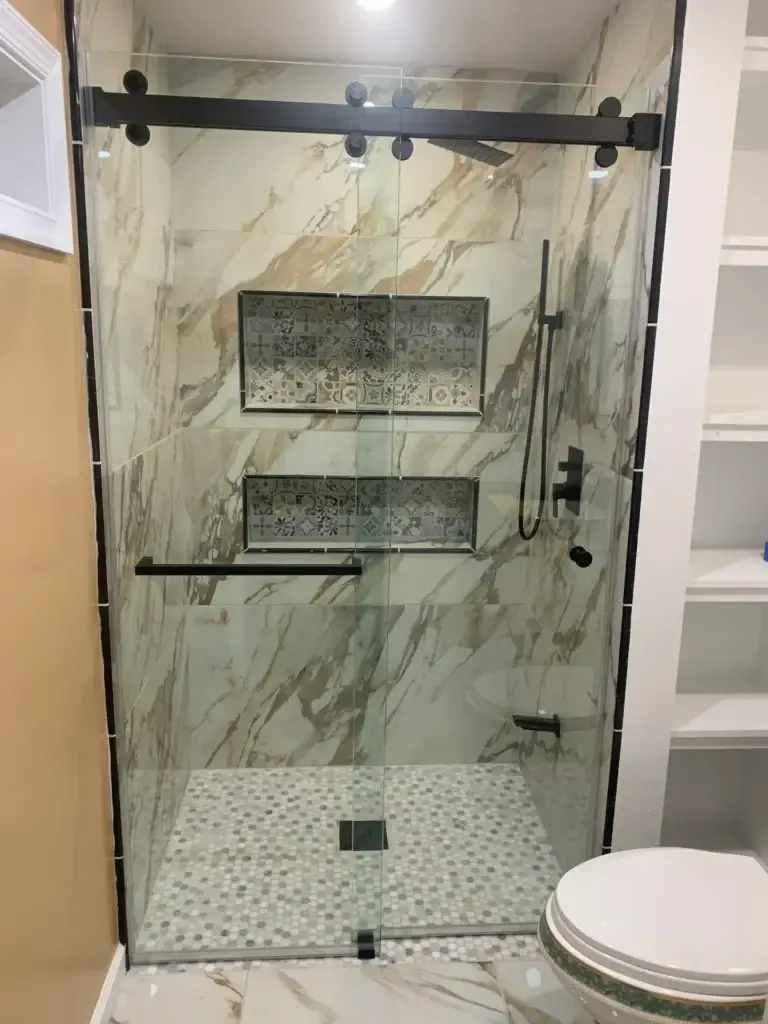 Frameless sliding shower door with matte black hardware in a gold-veined marble-look tile shower with patterned niches