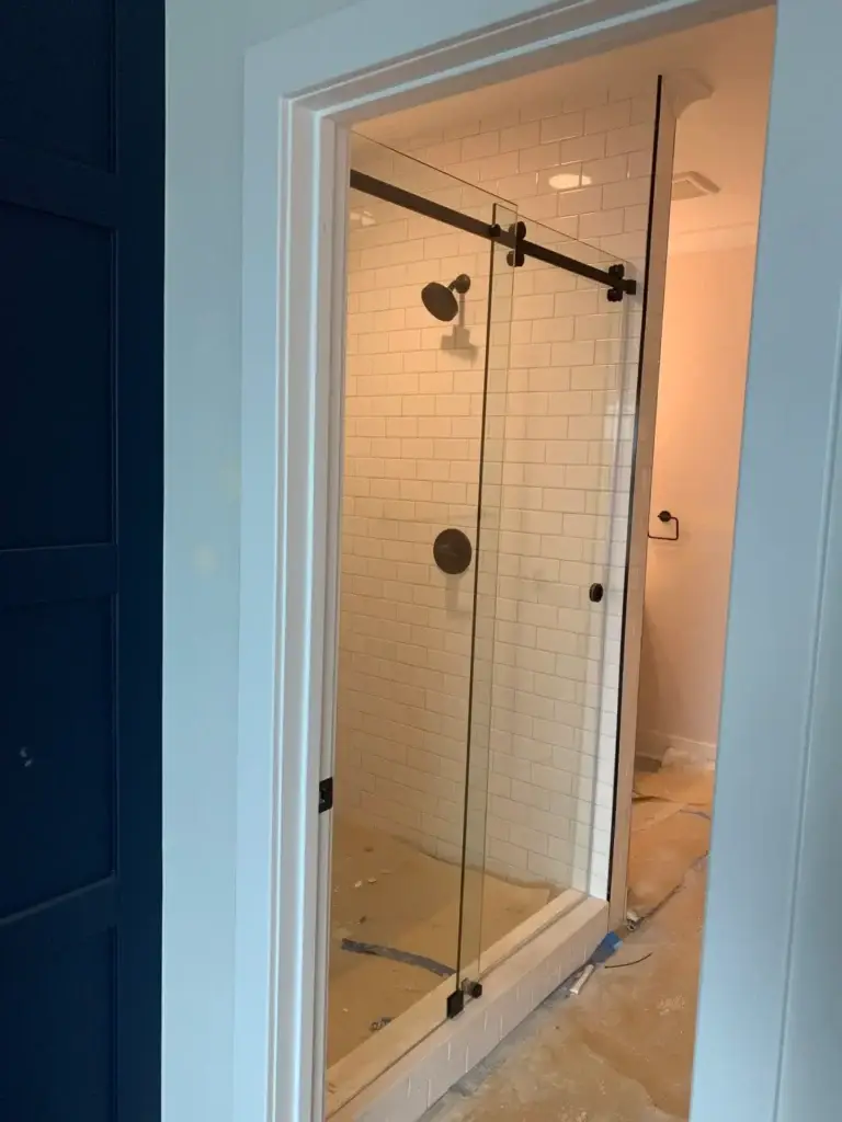 Frameless sliding shower door with matte black hardware in a white subway tile shower