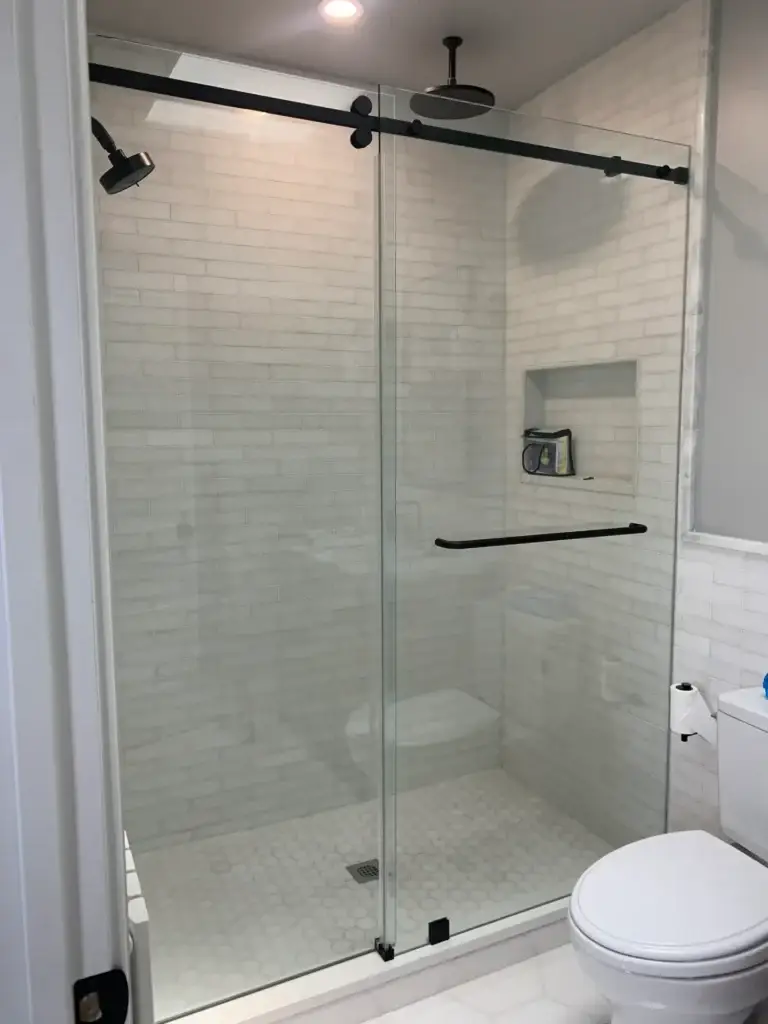 Frameless sliding shower door with a matte black rail and towel bar in a white subway tile shower