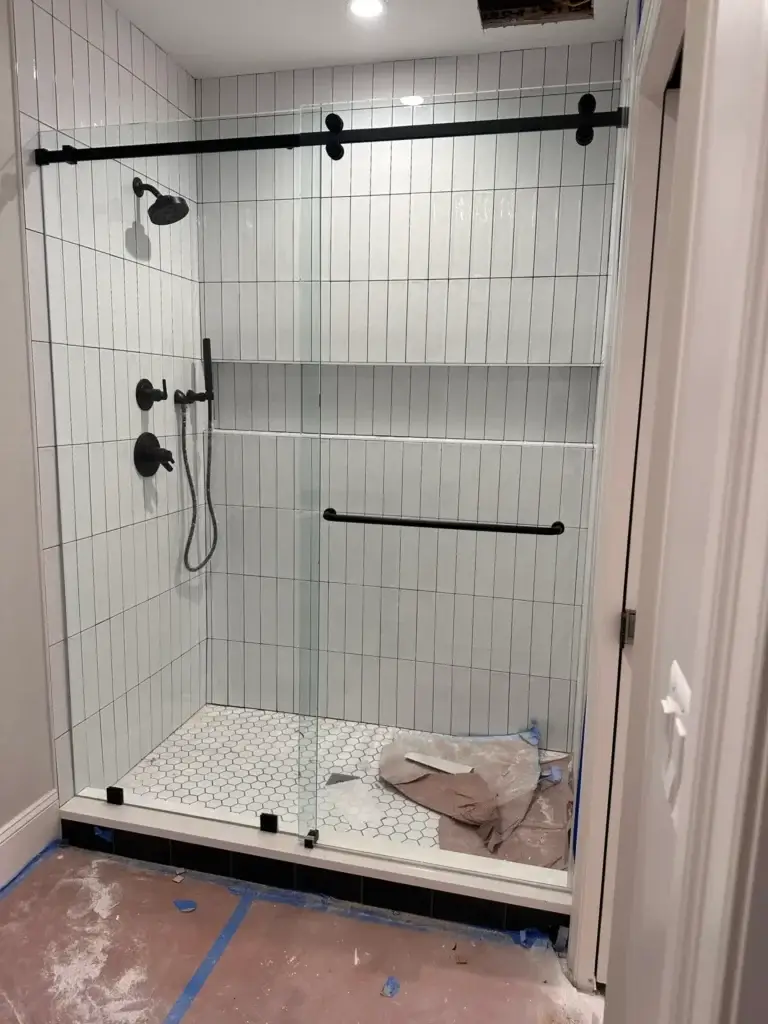 Frameless sliding shower door with matte black hardware in a white vertical stacked tile shower