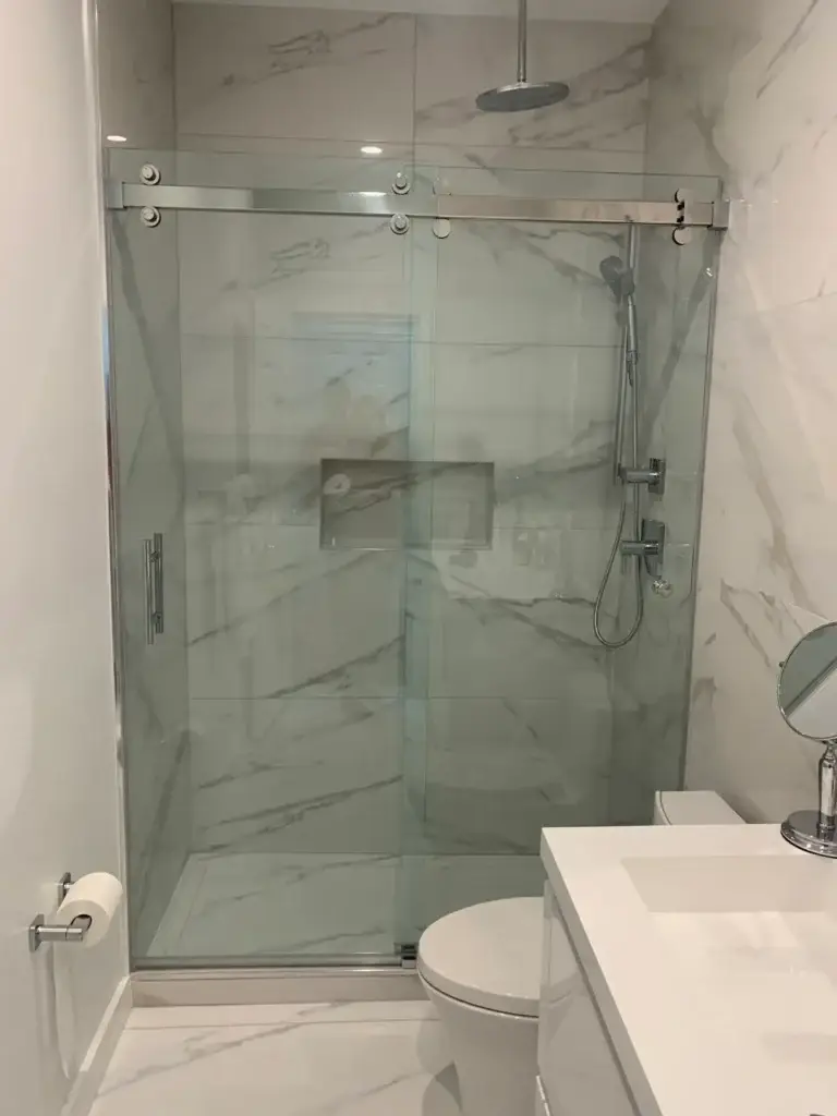 Frameless sliding shower door with a polished rail in a white marble-look tile shower