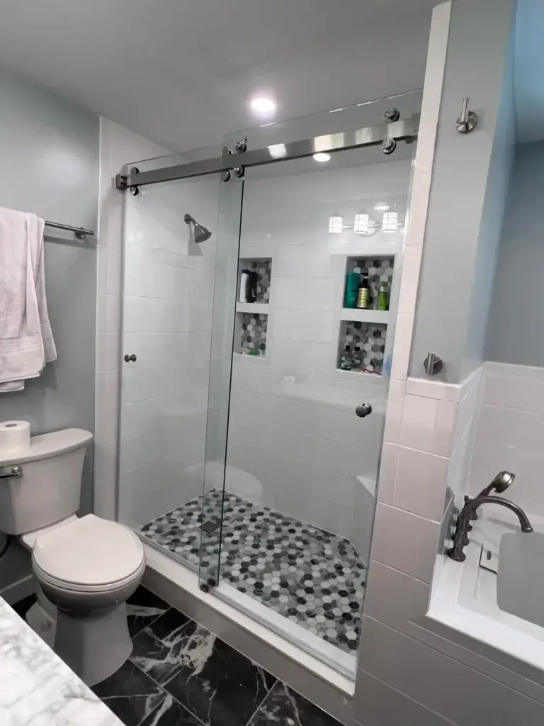 Frameless sliding shower door in a white tile shower with a grey hex mosaic floor