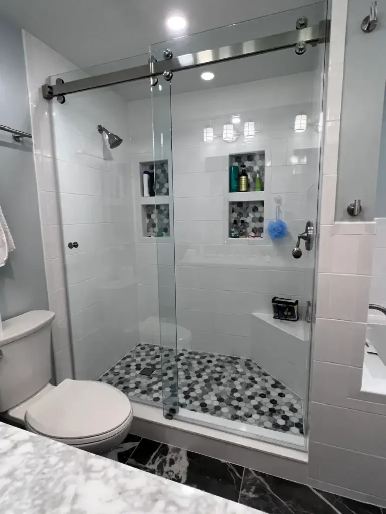 Frameless sliding shower door in a white tile shower with mosaic niches and a hex floor
