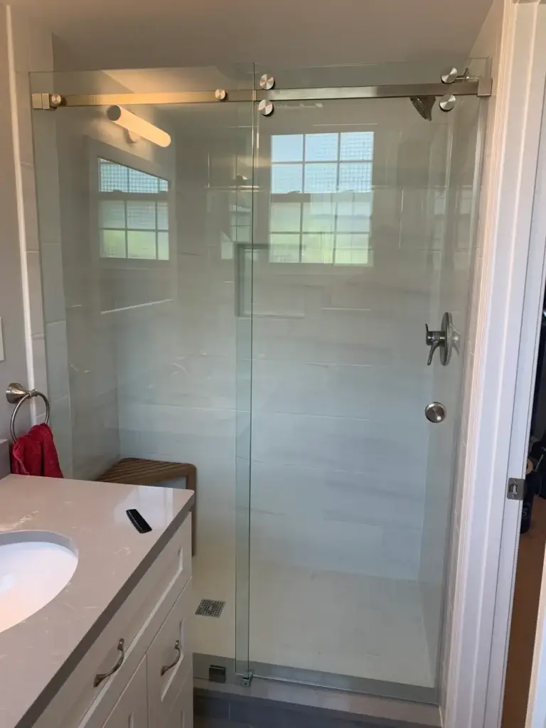 Frameless sliding shower door in a white tile shower with a window