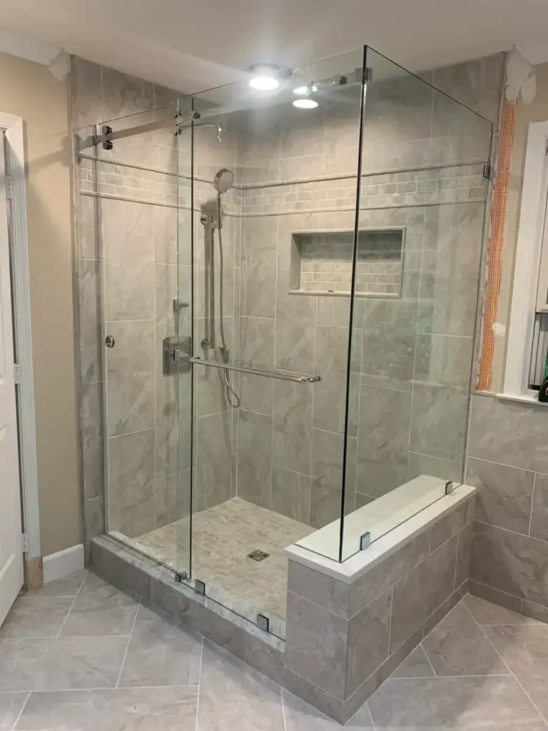 Frameless sliding shower enclosure with a return panel on a tiled bench in a grey tile corner shower