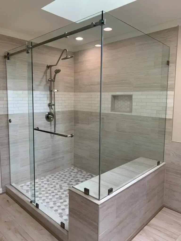 Frameless sliding shower enclosure over a tiled bench in a grey tile shower with a skylight