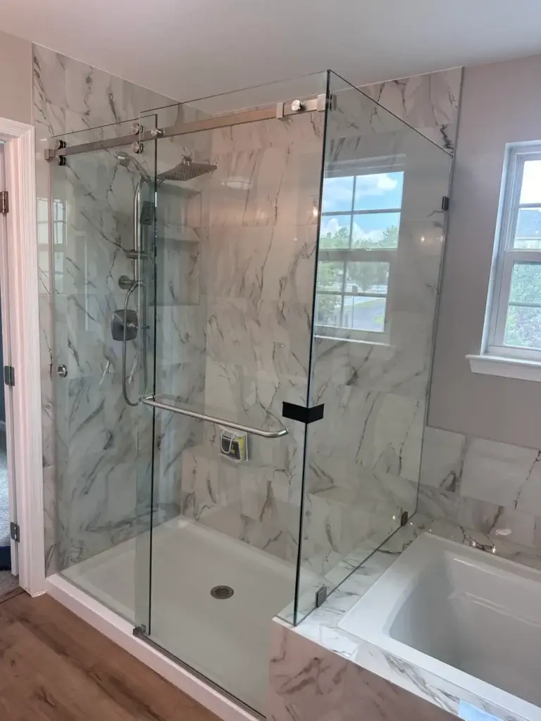 Frameless sliding shower enclosure with a return panel beside a bathtub in marble-look tile