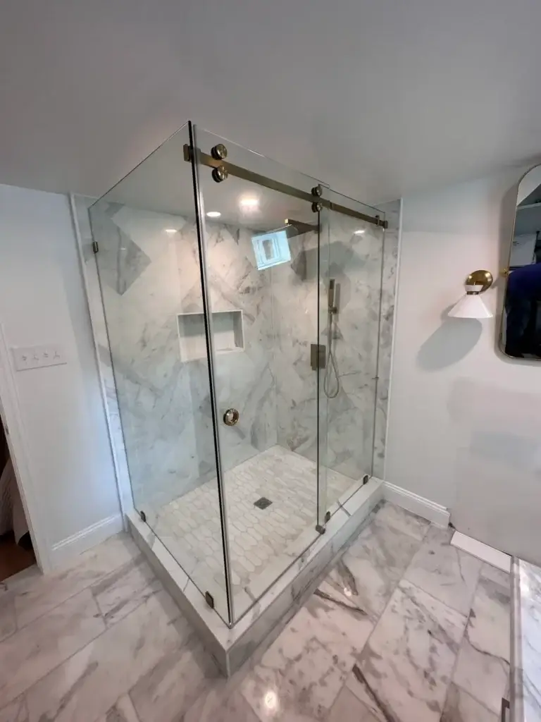 Frameless corner sliding shower enclosure with a gold-tone rail in a marble-look tile shower