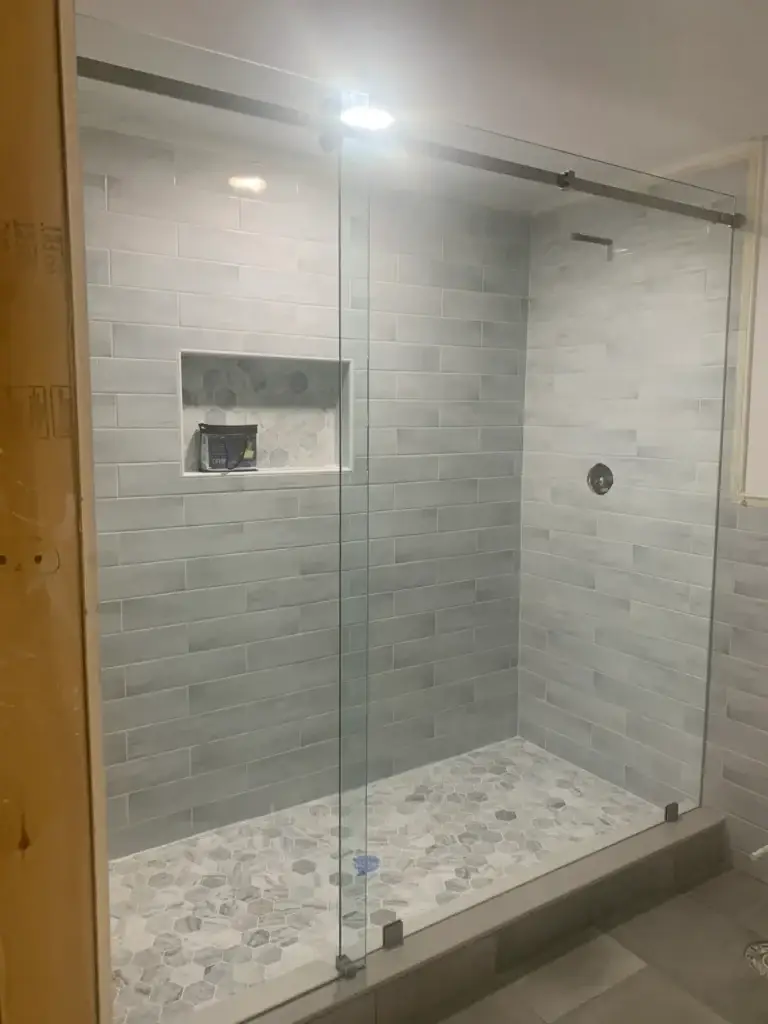 Frameless sliding shower enclosure with a return panel in a grey subway tile shower with a hex mosaic floor