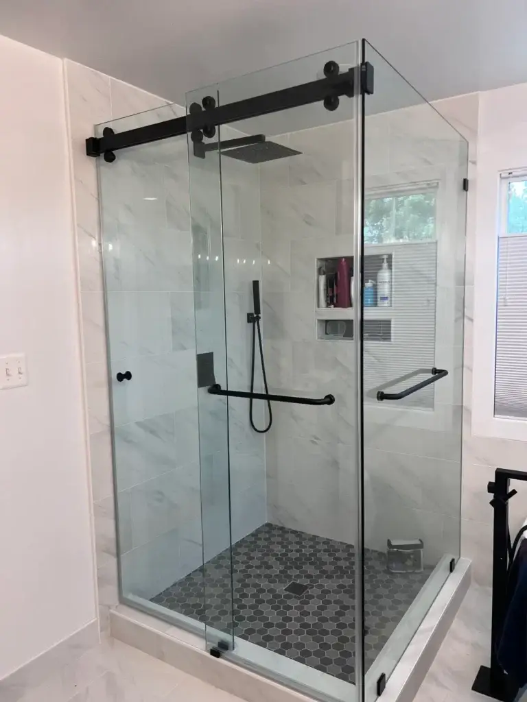 Frameless corner sliding shower enclosure with matte black hardware and a patterned mosaic floor