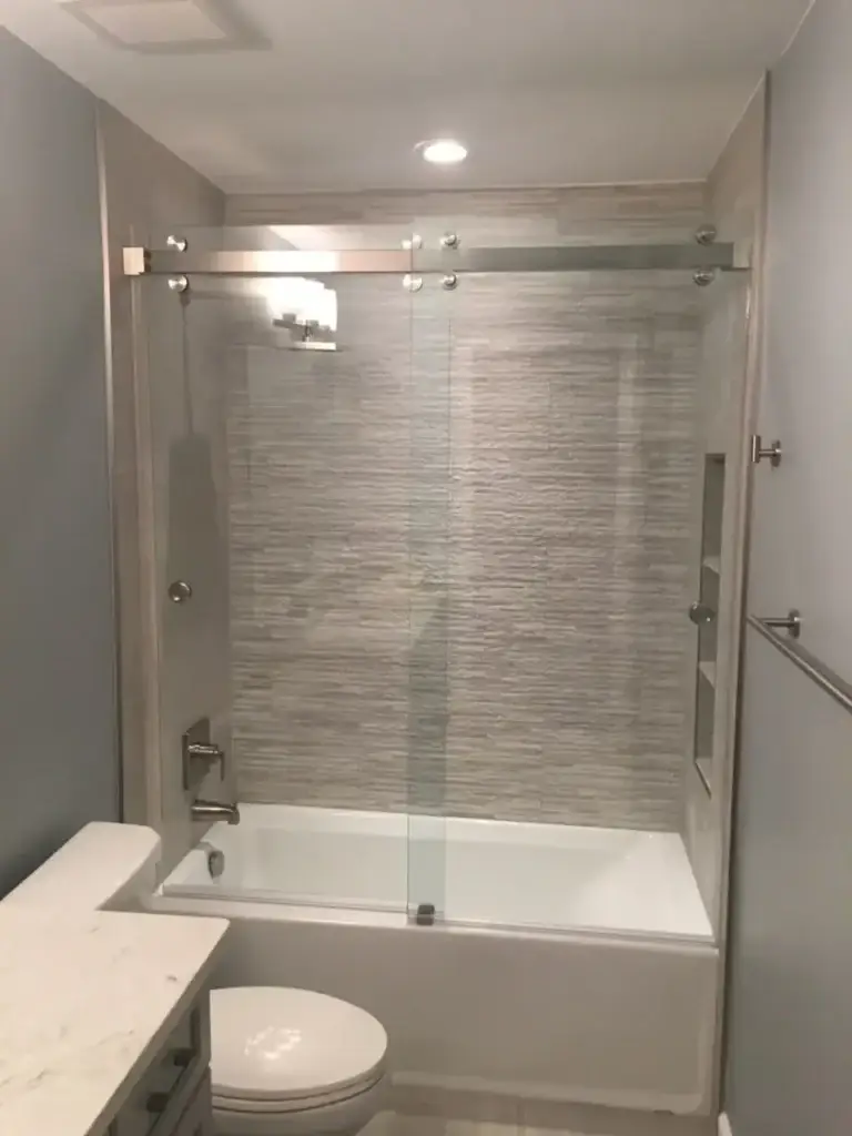 Frameless sliding glass door over a bathtub with grey textured tile
