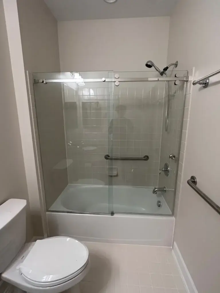 Frameless sliding glass door over a white tiled bathtub