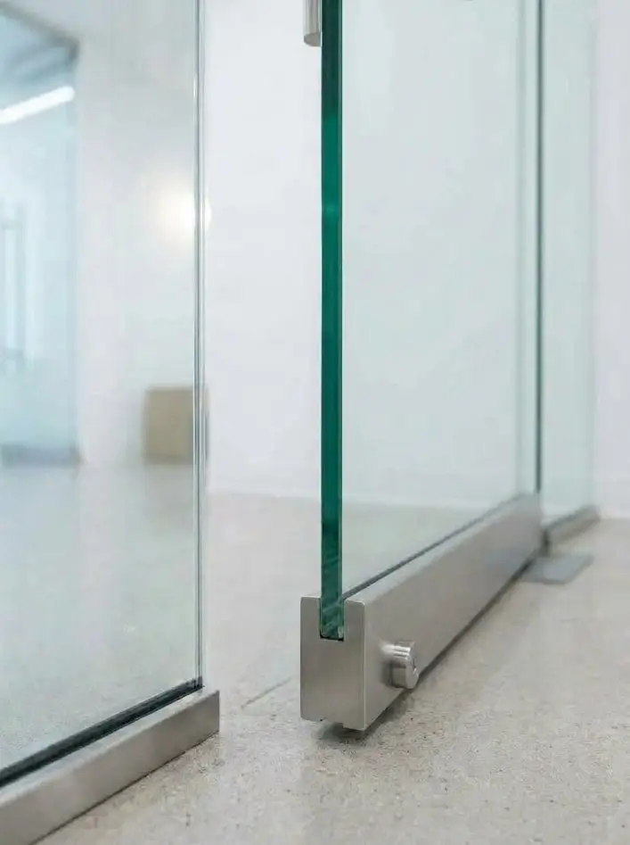 Close-up of a frameless glass door bottom rail with cylinder lock and floor channel
