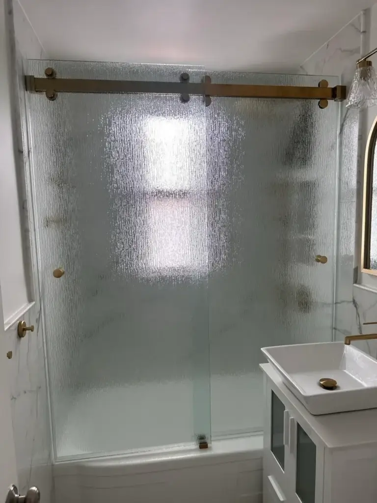 Sliding glass tub door with textured glass and a gold-tone rail