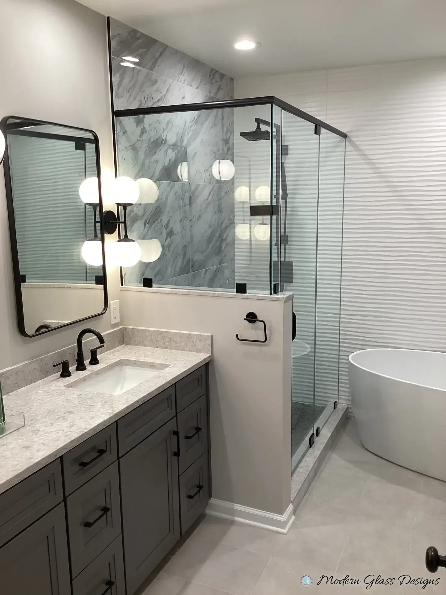 Frameless glass shower on a knee wall with black hardware in a grey marble-look bathroom