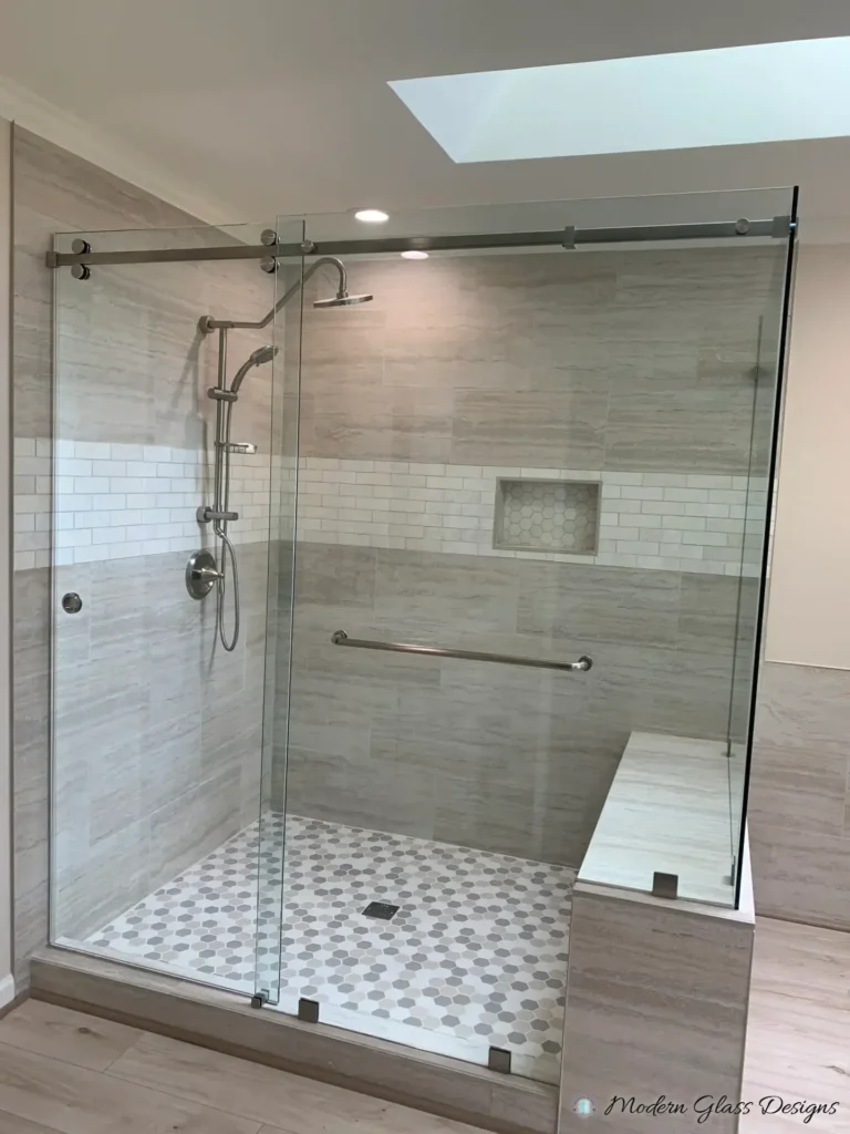 Frameless sliding shower door with a glass panel on a tiled bench, under a skylight