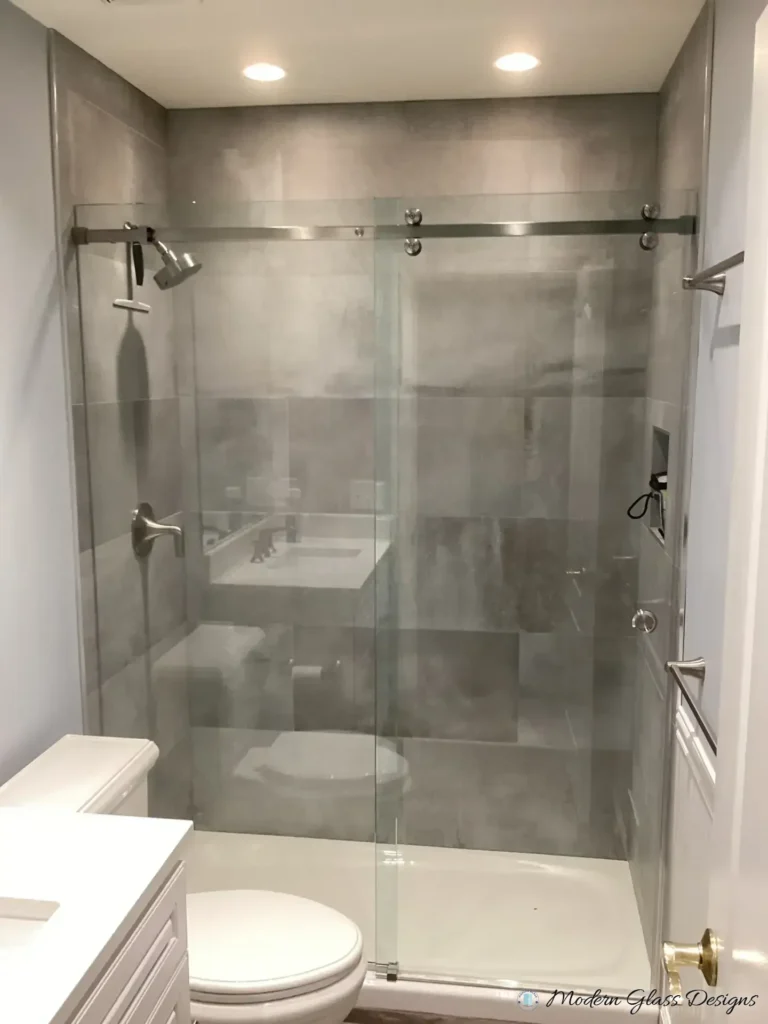 Frameless sliding shower door over a shower base in a grey large-format tile shower