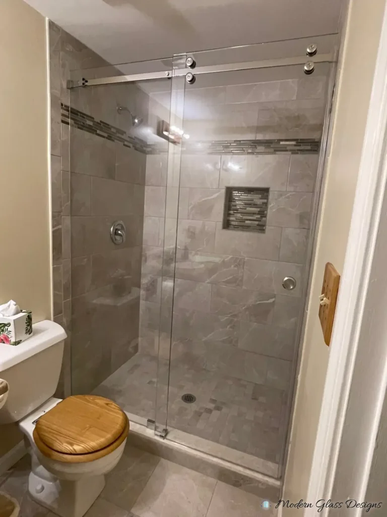 Frameless sliding shower door in a grey tile shower with a mosaic accent band