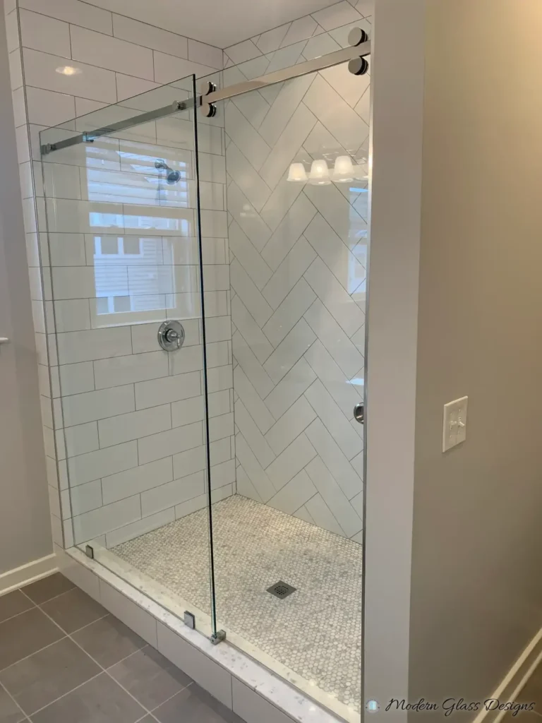 Frameless sliding shower door in a white herringbone subway tile shower with a mosaic floor