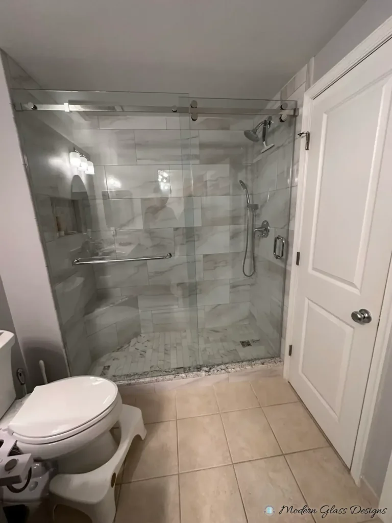 Frameless sliding shower door in a marble-look tile shower with a pebble floor