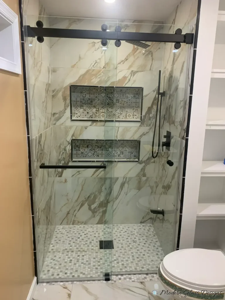Frameless sliding shower door with matte black hardware in a gold-veined marble-look tile shower with patterned niches