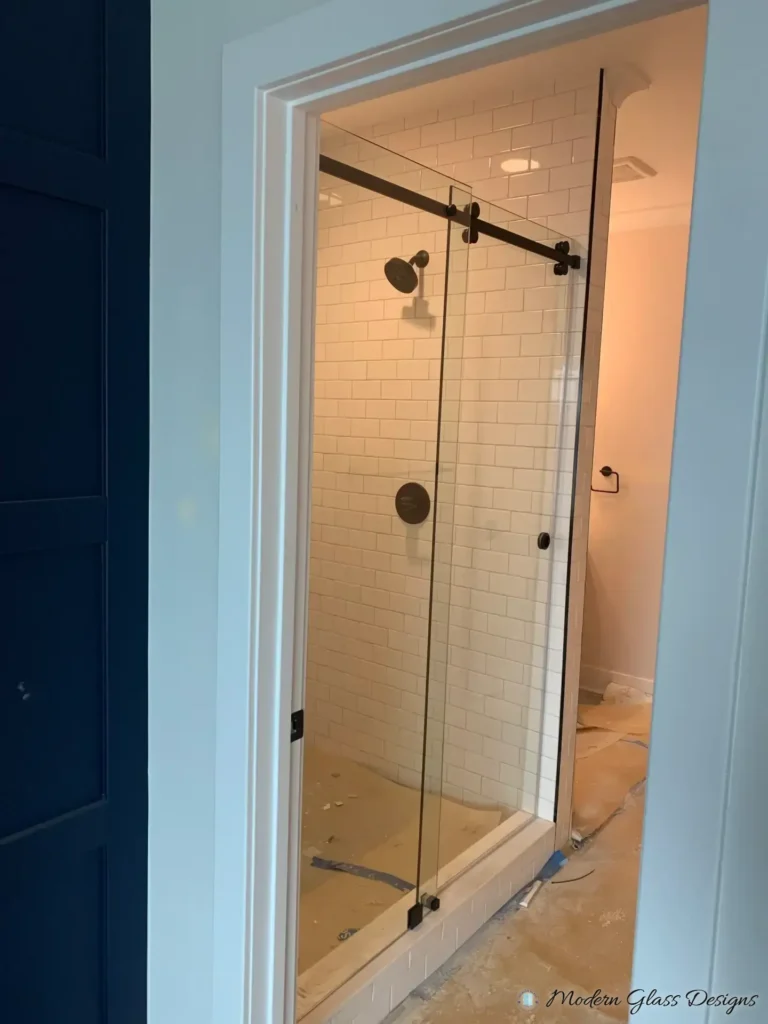 Frameless sliding shower door with matte black hardware in a white subway tile shower