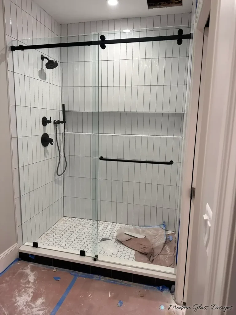Frameless sliding shower door with matte black hardware in a white vertical stacked tile shower