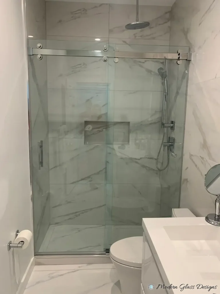 Frameless sliding shower door with a polished rail in a white marble-look tile shower