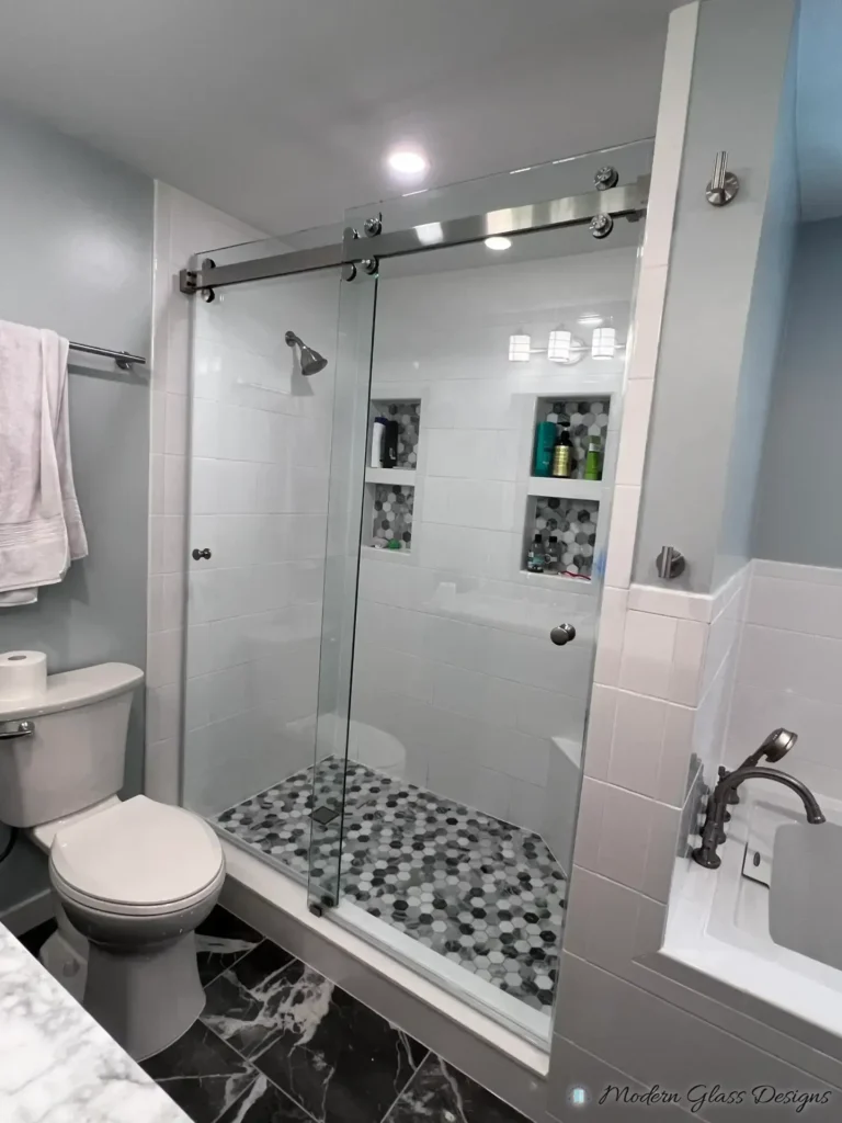 Frameless sliding shower door in a white tile shower with a grey hex mosaic floor