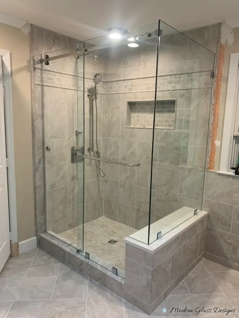 Frameless sliding shower enclosure with a return panel on a tiled bench in a grey tile corner shower