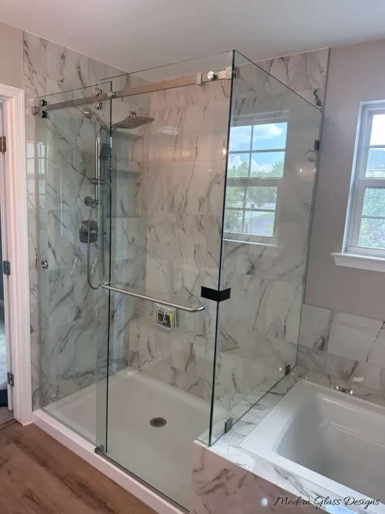 Frameless sliding shower enclosure with a return panel beside a bathtub in marble-look tile