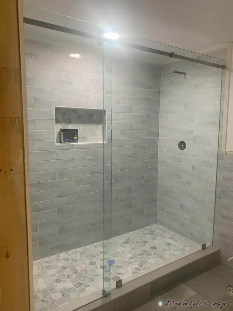 Frameless sliding shower enclosure with a return panel in a grey subway tile shower with a hex mosaic floor