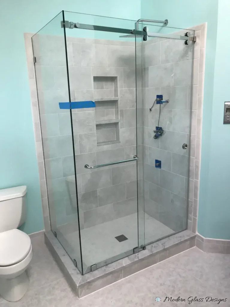 Frameless sliding shower enclosure with a return panel in a grey tile corner shower