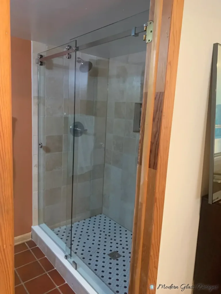 Frameless sliding shower enclosure with a return panel and a black-and-white hex mosaic floor