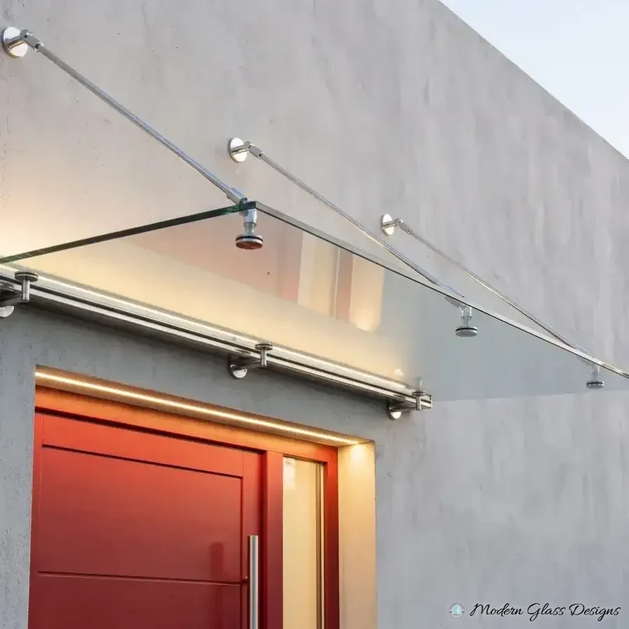 Frameless glass canopy with a lit wall rail and three steel rods above a red front door